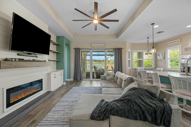 living room featuring dark wood-type flooring, ceiling fan, and a raised ceiling