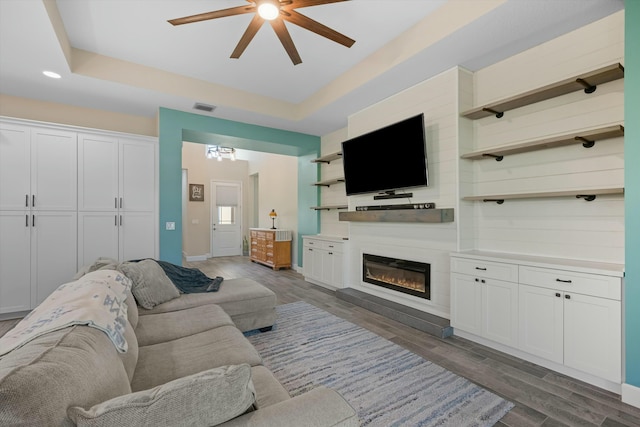 living room featuring a raised ceiling, dark hardwood / wood-style floors, and ceiling fan