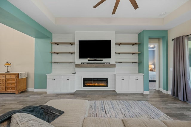 living room featuring a tray ceiling, ceiling fan, and light wood-type flooring