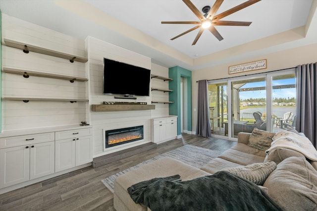 living room featuring dark hardwood / wood-style flooring, a raised ceiling, and ceiling fan