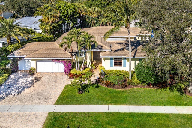 view of front of house featuring a garage, a tile roof, decorative driveway, a front yard, and stucco siding