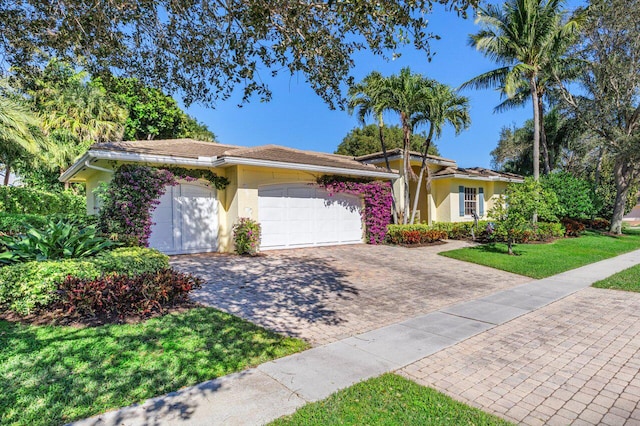 ranch-style home with a front yard, decorative driveway, an attached garage, and stucco siding