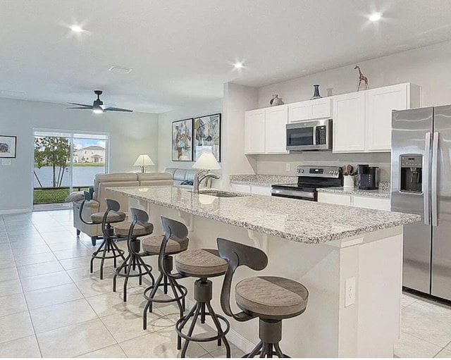 kitchen with open floor plan, a breakfast bar area, appliances with stainless steel finishes, white cabinets, and a sink