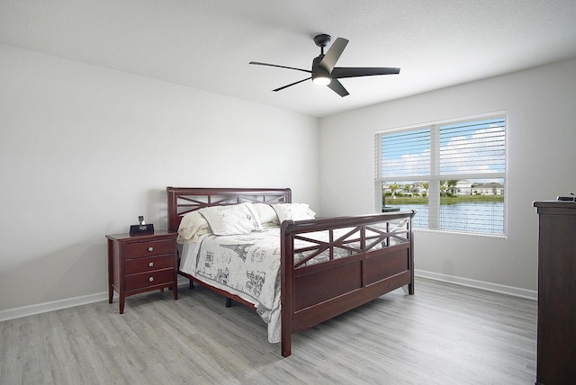 bedroom with light hardwood / wood-style floors, ceiling fan, and a water view