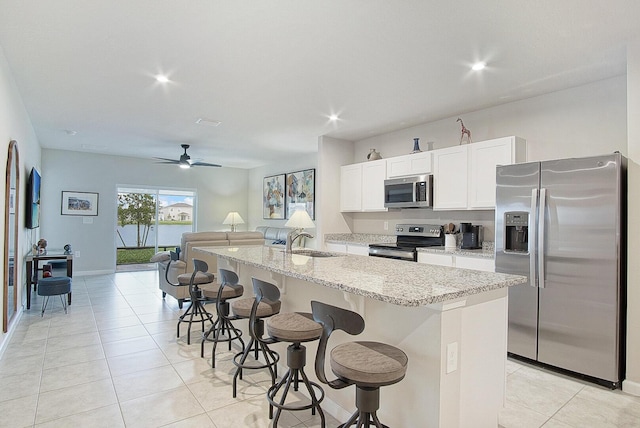 kitchen with appliances with stainless steel finishes, a kitchen island with sink, a sink, white cabinetry, and a kitchen breakfast bar