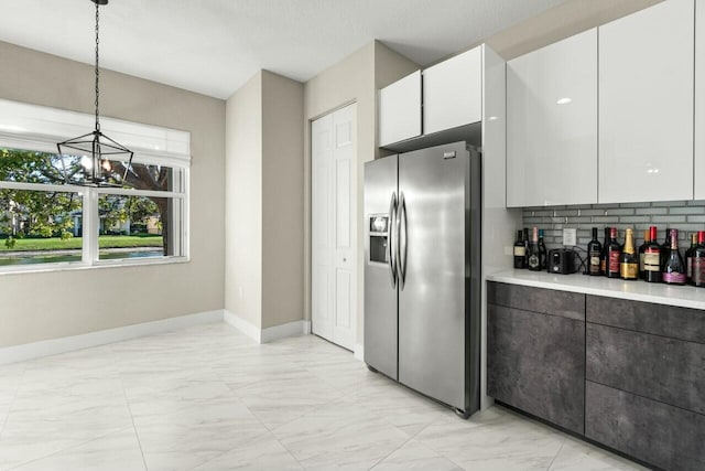 kitchen featuring pendant lighting, white cabinets, backsplash, stainless steel refrigerator with ice dispenser, and an inviting chandelier