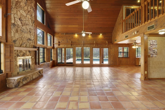 unfurnished living room with wood ceiling, ceiling fan, high vaulted ceiling, a fireplace, and wood walls