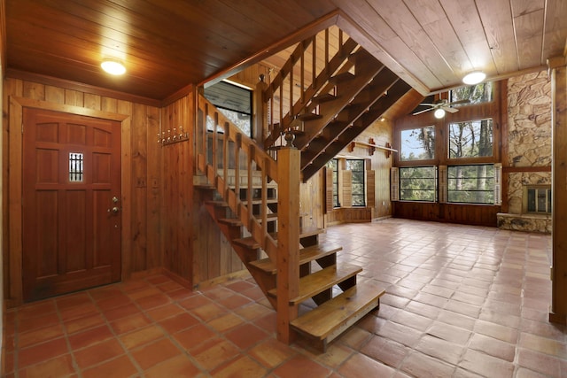 entryway with a stone fireplace, high vaulted ceiling, wooden walls, ceiling fan, and wooden ceiling