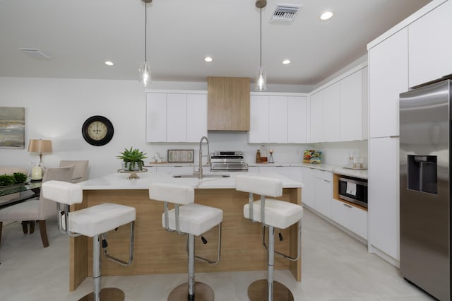 kitchen with pendant lighting, a kitchen island with sink, white cabinets, and appliances with stainless steel finishes