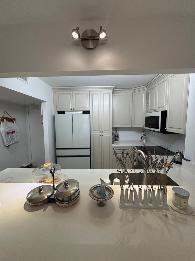 kitchen with white fridge, white cabinets, and backsplash