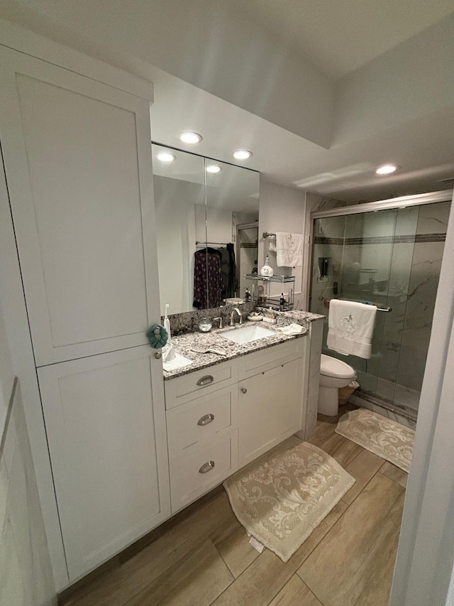 bathroom with a shower with door, vanity, and toilet