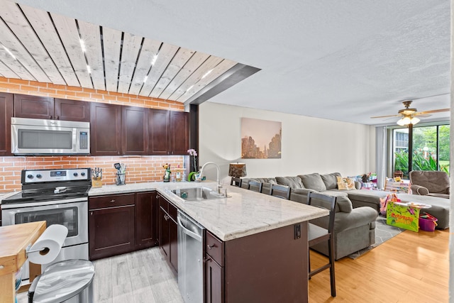 kitchen with stainless steel appliances, kitchen peninsula, sink, and light hardwood / wood-style flooring