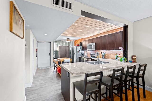 kitchen featuring a kitchen bar, tasteful backsplash, kitchen peninsula, stainless steel appliances, and light stone countertops