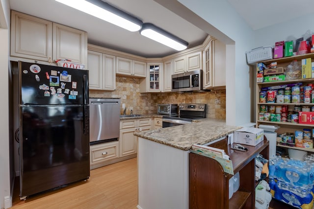 kitchen with a peninsula, appliances with stainless steel finishes, and cream cabinetry