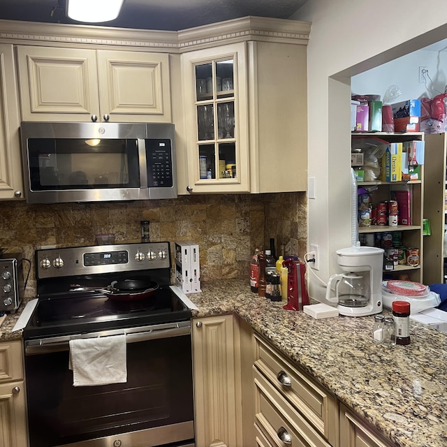 kitchen with appliances with stainless steel finishes, backsplash, and cream cabinetry