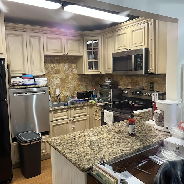 kitchen featuring sink, stone counters, stainless steel appliances, cream cabinets, and backsplash