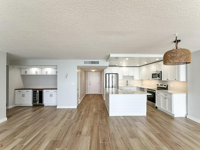 kitchen featuring pendant lighting, appliances with stainless steel finishes, white cabinetry, beverage cooler, and light wood-type flooring