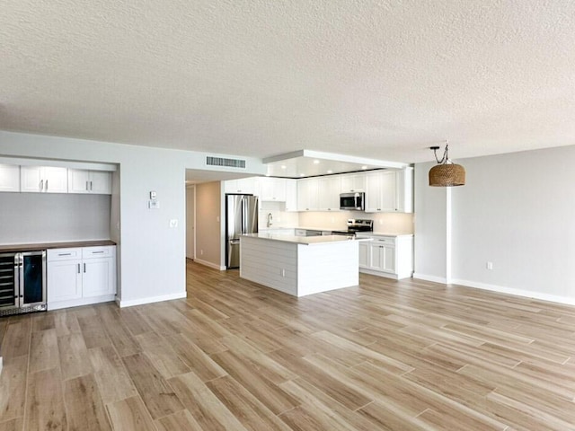 kitchen with white cabinetry, pendant lighting, stainless steel appliances, beverage cooler, and light hardwood / wood-style floors