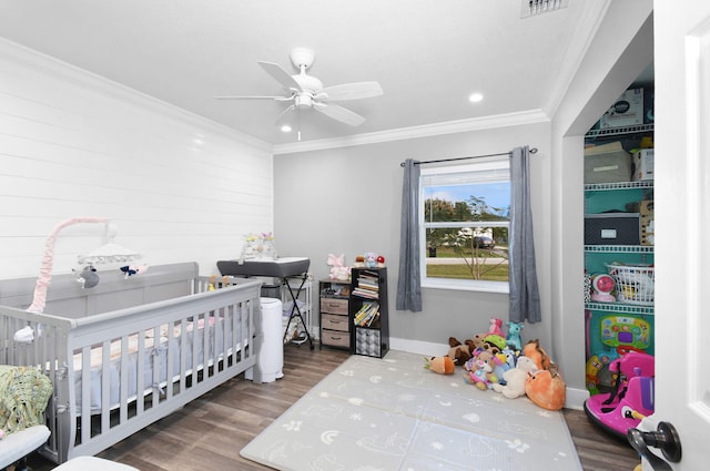 bedroom featuring hardwood / wood-style flooring, ornamental molding, a crib, and ceiling fan