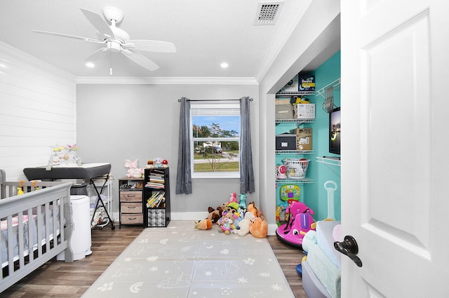 bedroom with ornamental molding, a nursery area, dark hardwood / wood-style floors, and ceiling fan