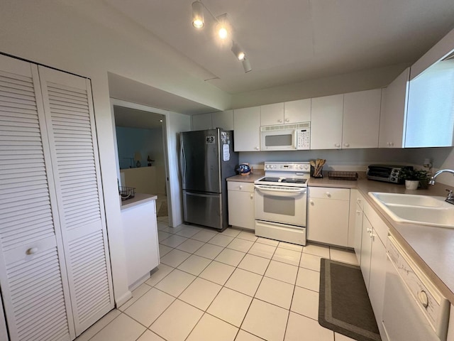 kitchen with sink, white appliances, light tile patterned floors, and white cabinets