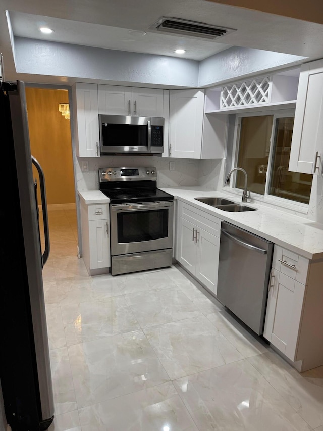 kitchen with white cabinetry, stainless steel appliances, light stone countertops, and sink