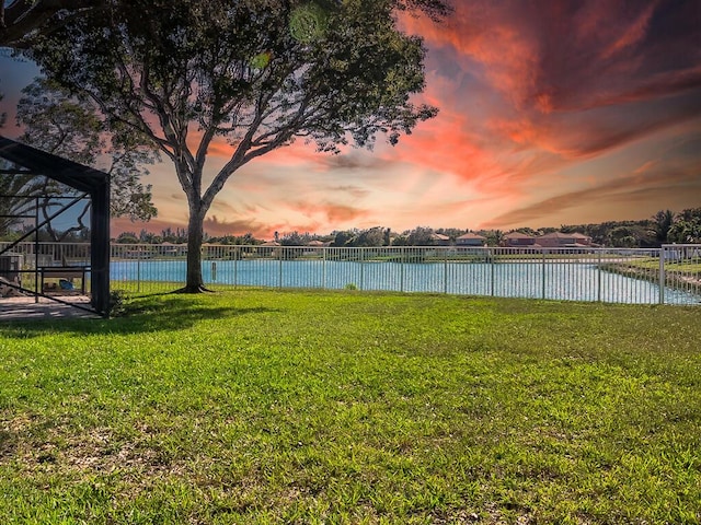 yard at dusk with a water view and glass enclosure