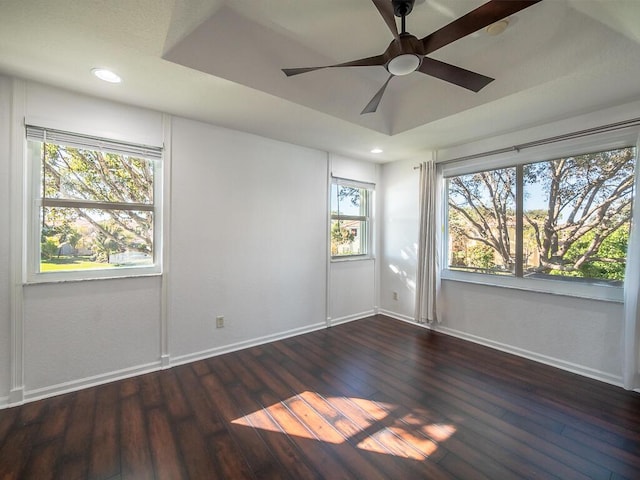 empty room with dark wood-type flooring, a raised ceiling, and ceiling fan