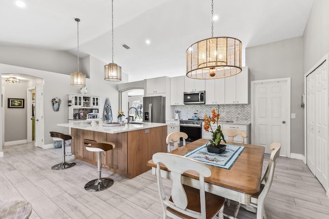 kitchen featuring decorative light fixtures, a center island with sink, white cabinets, stainless steel appliances, and backsplash