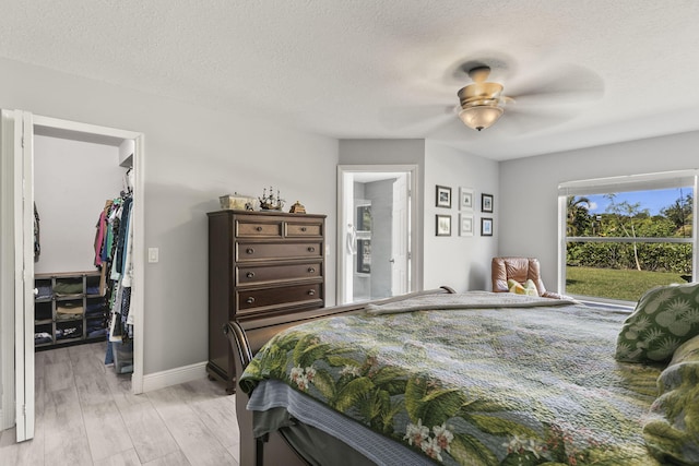 bedroom featuring light wood-type flooring, a walk in closet, ceiling fan, a textured ceiling, and a closet