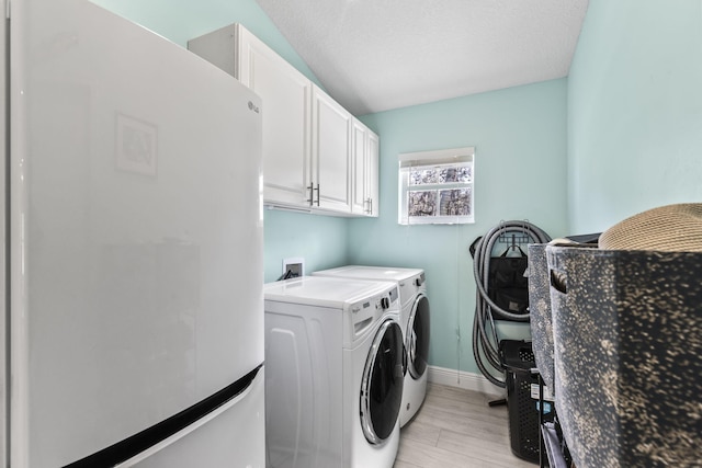 laundry area with cabinets, washing machine and dryer, a textured ceiling, and light hardwood / wood-style flooring