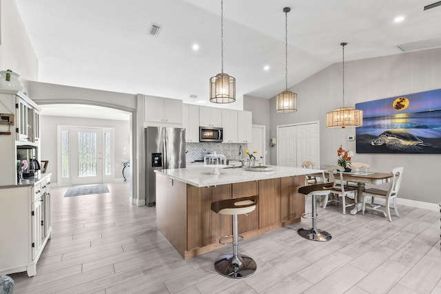 kitchen with white cabinetry, hanging light fixtures, a kitchen island with sink, stainless steel appliances, and light stone countertops