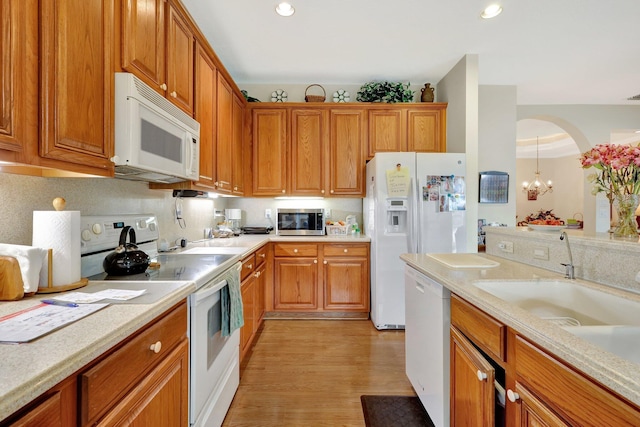 kitchen with sink, a chandelier, light wood-type flooring, white appliances, and decorative backsplash