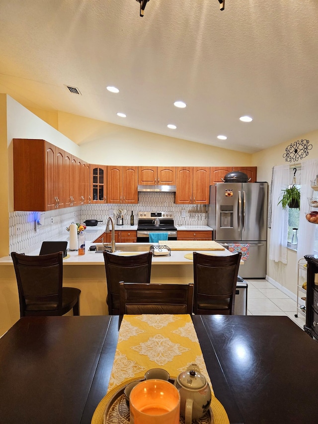 kitchen featuring tasteful backsplash, lofted ceiling, stainless steel appliances, and light tile patterned flooring