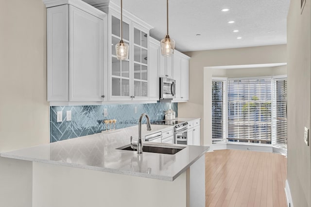 kitchen featuring sink, white cabinets, backsplash, hanging light fixtures, and kitchen peninsula