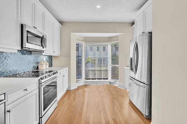 kitchen with stainless steel appliances, white cabinetry, light hardwood / wood-style flooring, and decorative backsplash