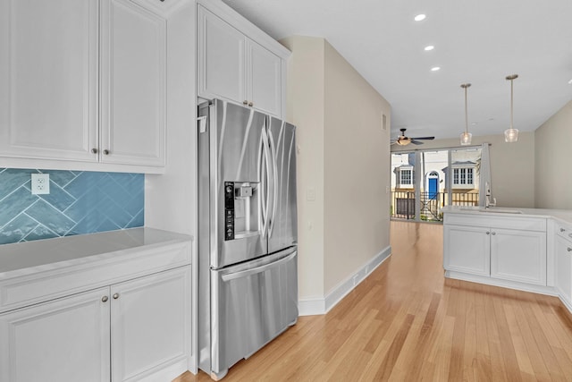 kitchen featuring decorative light fixtures, stainless steel fridge with ice dispenser, light wood-type flooring, decorative backsplash, and white cabinets