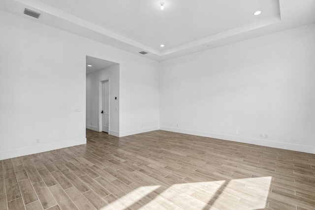 spare room featuring a tray ceiling and light hardwood / wood-style floors