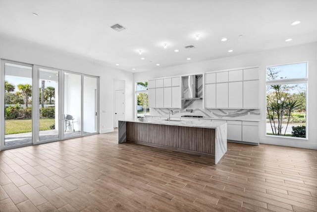 kitchen with sink, white cabinets, wall chimney range hood, a large island, and backsplash