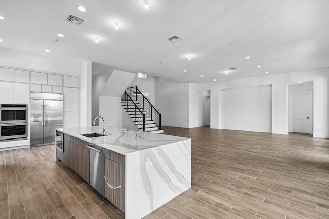 kitchen with light stone counters, appliances with stainless steel finishes, a large island, and sink