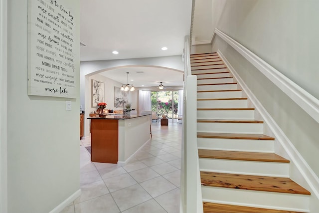 staircase featuring tile patterned floors, baseboards, ceiling fan, recessed lighting, and arched walkways