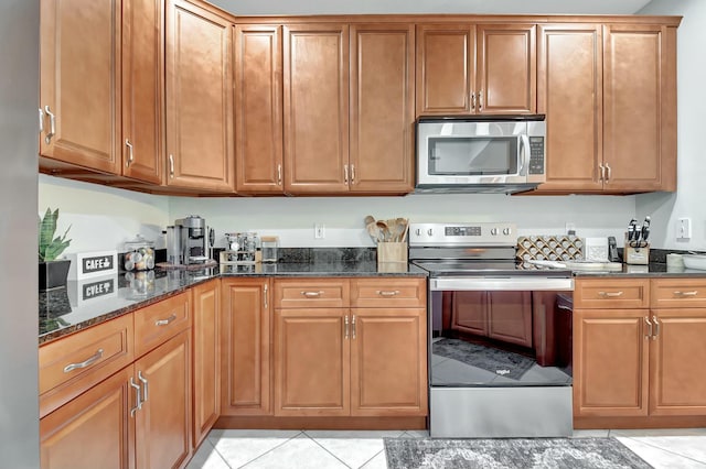 kitchen with appliances with stainless steel finishes, dark stone countertops, and light tile patterned floors