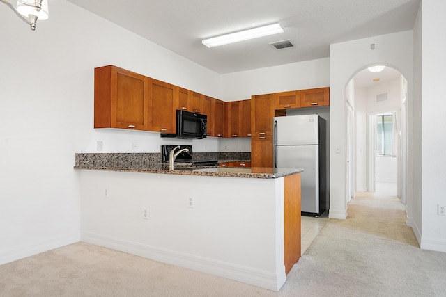 kitchen featuring dark stone counters, light colored carpet, stainless steel refrigerator, and kitchen peninsula