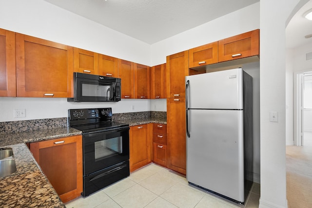 kitchen featuring dark stone countertops, light tile patterned floors, and black appliances