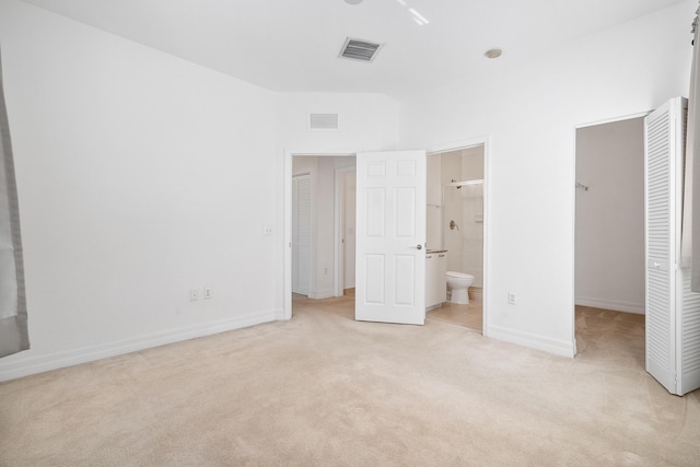 unfurnished bedroom featuring light carpet, connected bathroom, a walk in closet, and a closet