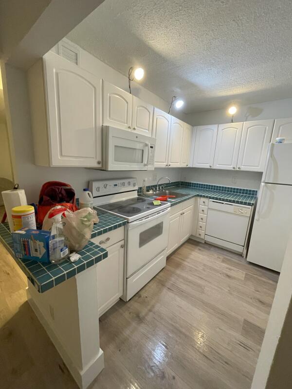 kitchen with white cabinetry, white appliances, tile counters, and light hardwood / wood-style floors