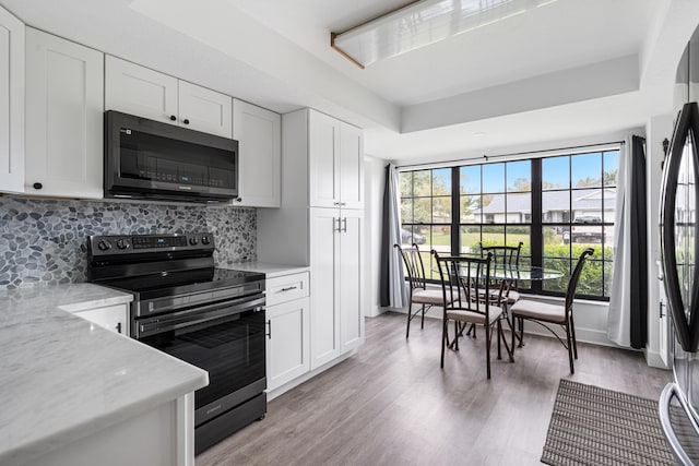 kitchen with tasteful backsplash, light wood-type flooring, electric range, light stone countertops, and white cabinets