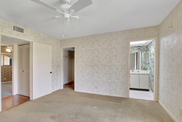 unfurnished bedroom with ensuite bathroom, light carpet, ceiling fan, and a textured ceiling