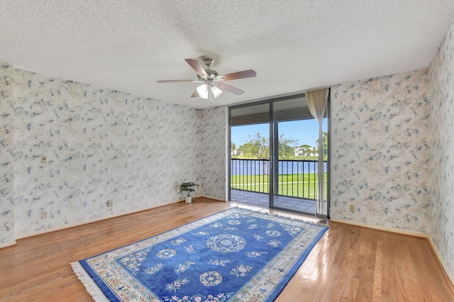 unfurnished room featuring ceiling fan, wood-type flooring, a textured ceiling, and a water view