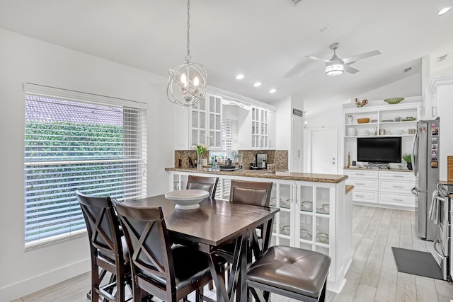 dining space with ceiling fan with notable chandelier, vaulted ceiling, and light wood-type flooring